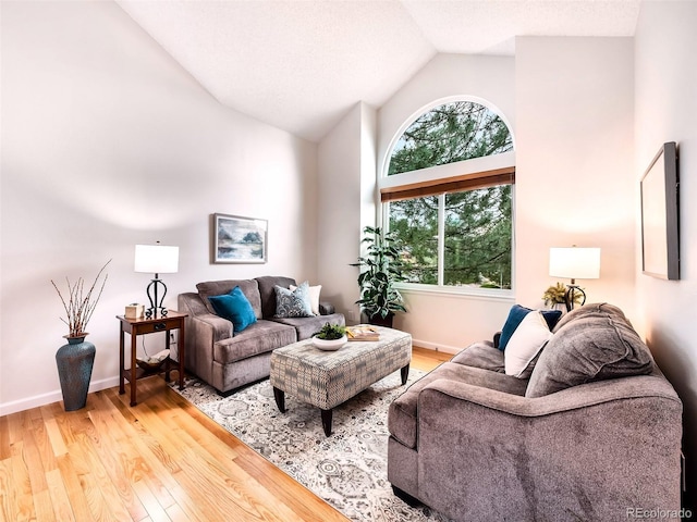 living area with high vaulted ceiling, baseboards, and wood finished floors