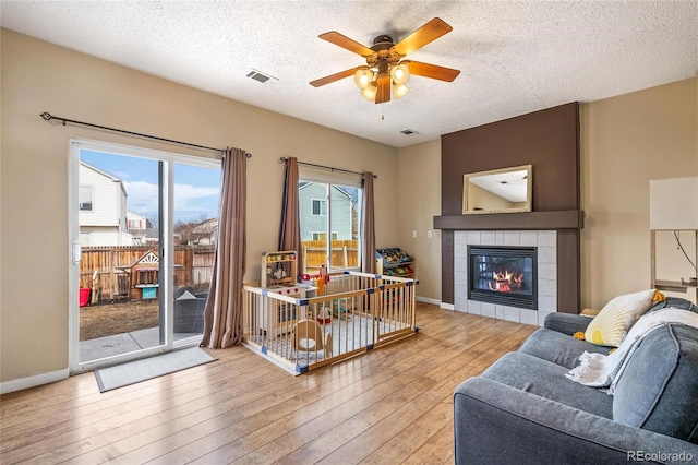 living room featuring a tiled fireplace, wood-type flooring, a textured ceiling, and ceiling fan