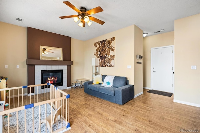 living room featuring hardwood / wood-style flooring, ceiling fan, a fireplace, and a textured ceiling