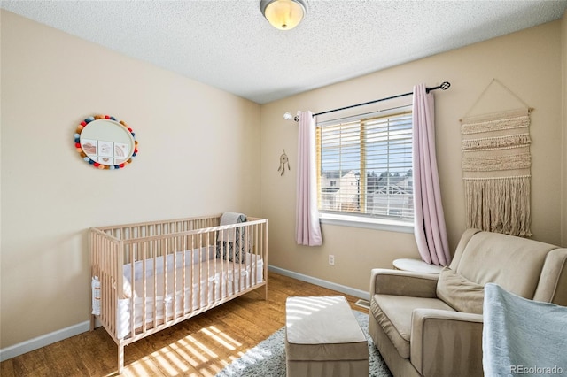 bedroom with hardwood / wood-style flooring, a nursery area, and a textured ceiling