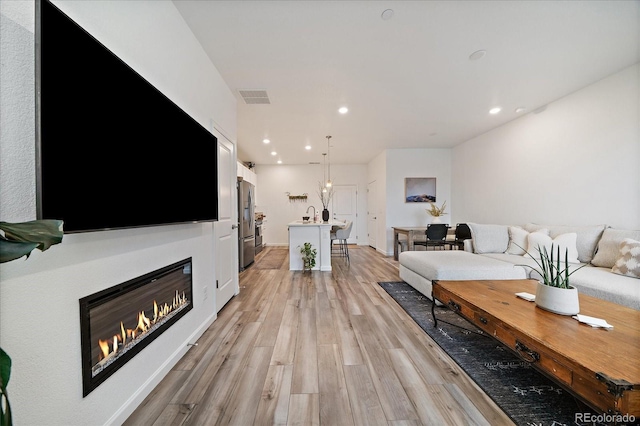 living area with light wood-type flooring, recessed lighting, and a glass covered fireplace
