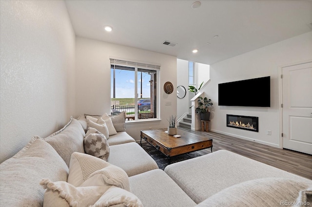 living area featuring wood finished floors, a glass covered fireplace, recessed lighting, stairway, and baseboards
