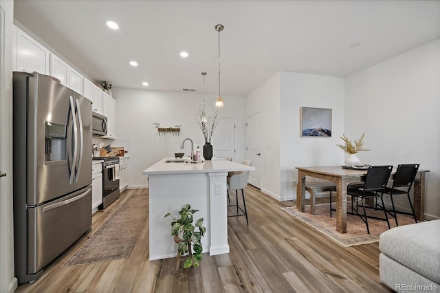 kitchen with appliances with stainless steel finishes, a sink, white cabinetry, a kitchen bar, and light wood-type flooring