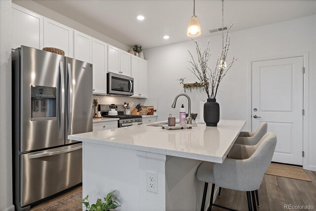 kitchen featuring appliances with stainless steel finishes, a sink, recessed lighting, a kitchen island with sink, and white cabinets