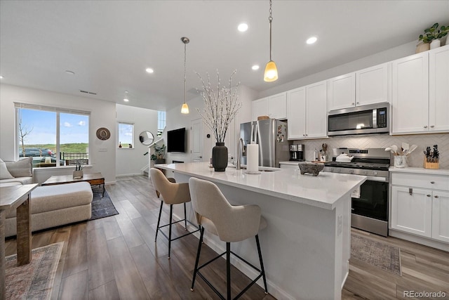 kitchen with appliances with stainless steel finishes, open floor plan, tasteful backsplash, a kitchen island with sink, and white cabinetry