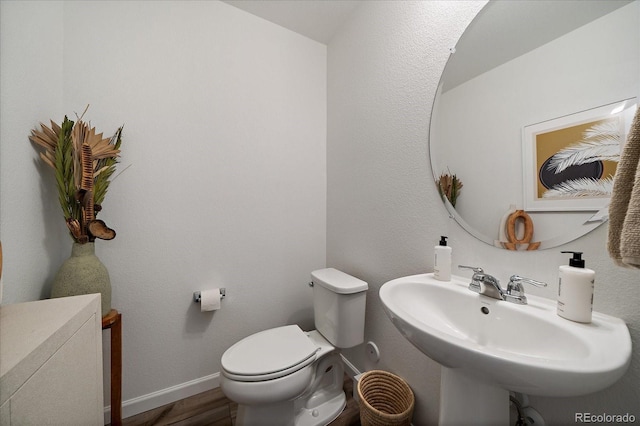 half bathroom featuring toilet, wood finished floors, and a sink