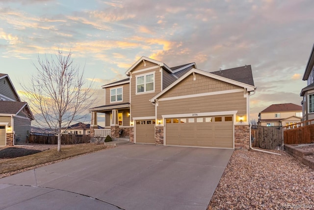 craftsman-style home with driveway, a garage, stone siding, covered porch, and fence