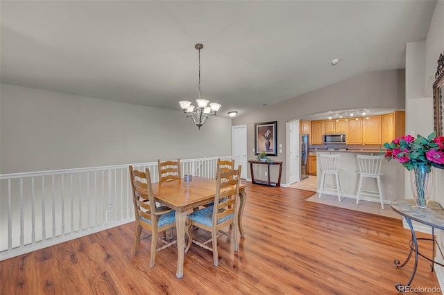 dining space with lofted ceiling, a chandelier, and light wood-type flooring