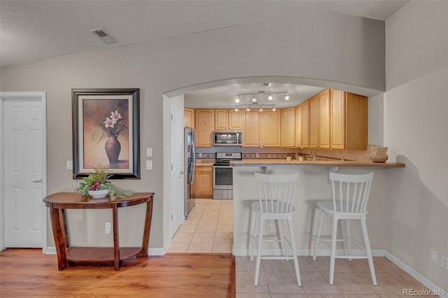 kitchen featuring tasteful backsplash, light brown cabinetry, stainless steel appliances, lofted ceiling, and light tile patterned floors