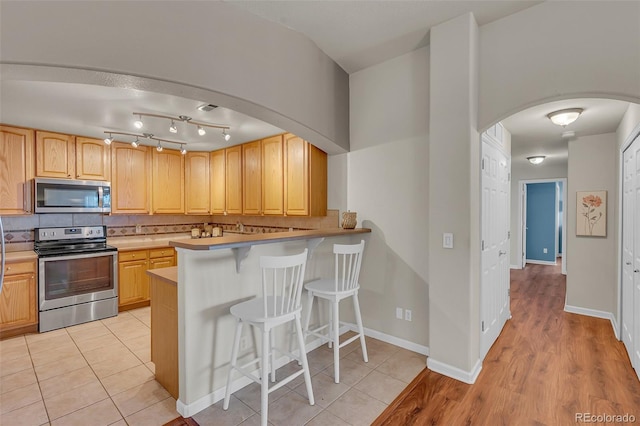 kitchen featuring light brown cabinets, stainless steel appliances, a kitchen bar, and backsplash