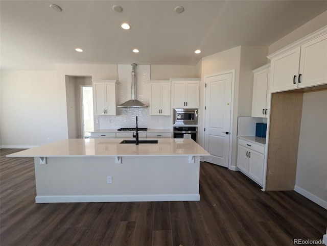 kitchen featuring white cabinets, stainless steel appliances, wall chimney exhaust hood, and an island with sink