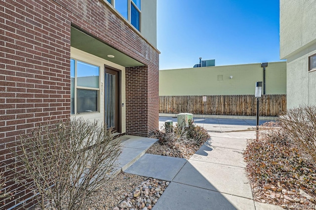 view of exterior entry with brick siding and fence