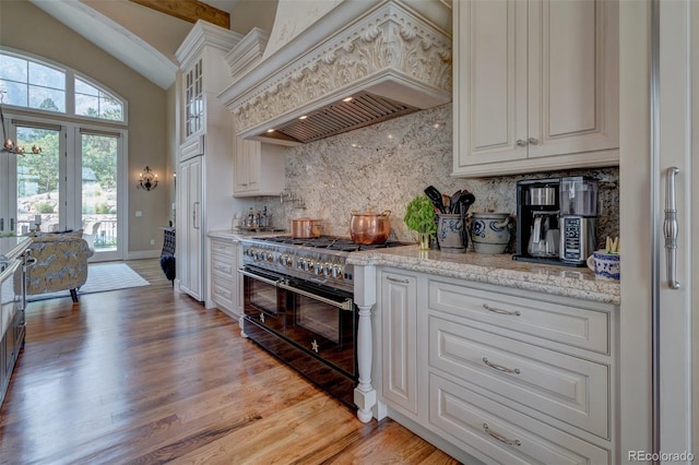 kitchen featuring premium range hood, backsplash, white cabinets, and double oven range