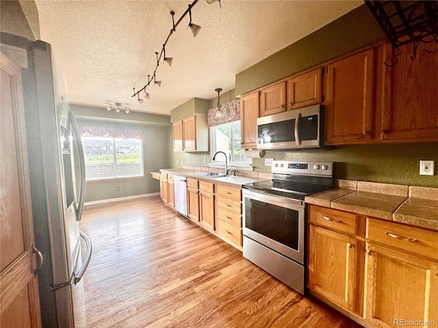 10064 Westside Cir, Littleton, CO 80125 - kitchen with appliances with stainless steel finishes, a textured ceiling, rail lighting, light wood-type flooring, and brown cabinetry