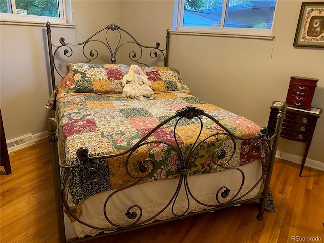 bedroom with wood finished floors, visible vents, and baseboards