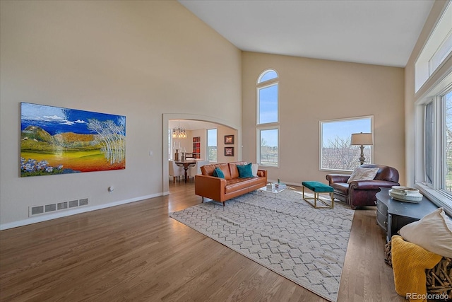 living room with wood finished floors, arched walkways, baseboards, a high ceiling, and visible vents