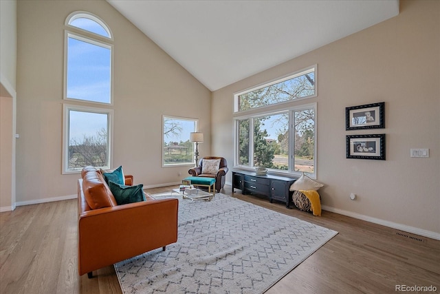 living area featuring baseboards, light wood-style flooring, visible vents, and high vaulted ceiling