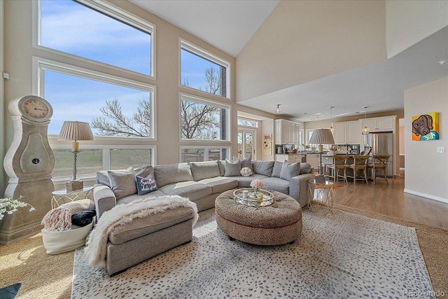 living area with baseboards, wood finished floors, a wealth of natural light, and high vaulted ceiling