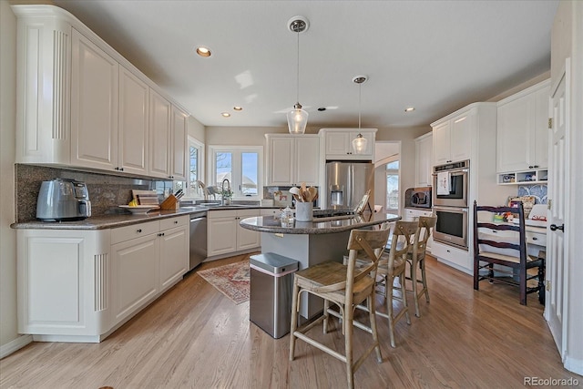 kitchen with a kitchen bar, light wood-type flooring, a kitchen island, and appliances with stainless steel finishes
