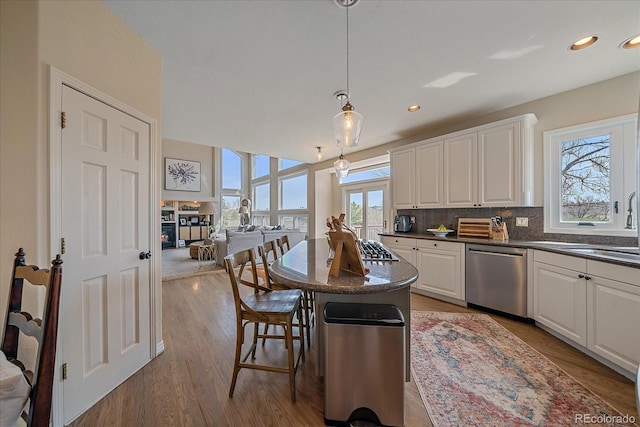 kitchen with white cabinets, stainless steel dishwasher, a sink, decorative backsplash, and a breakfast bar area