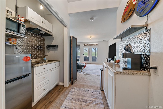 kitchen featuring a sink, light wood-style floors, stainless steel appliances, backsplash, and white cabinetry