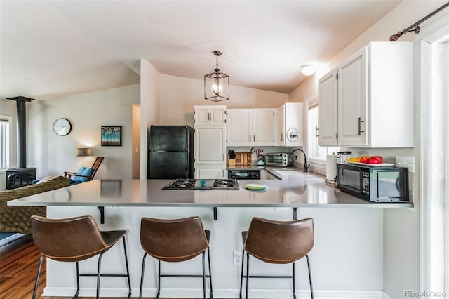 7256 Aspen Meadow Dr, Evergreen, CO 80439 - kitchen featuring black appliances, a wood stove, a peninsula, lofted ceiling, and white cabinetry