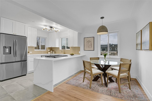 kitchen featuring a peninsula, stainless steel fridge with ice dispenser, light countertops, white cabinetry, and a notable chandelier