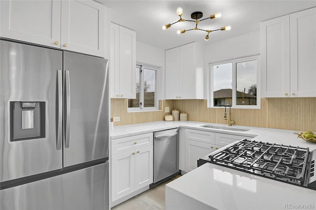 kitchen with light countertops, appliances with stainless steel finishes, an inviting chandelier, white cabinets, and a sink