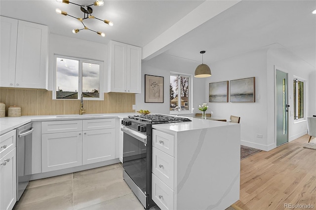 kitchen with appliances with stainless steel finishes, a peninsula, a notable chandelier, white cabinetry, and a sink