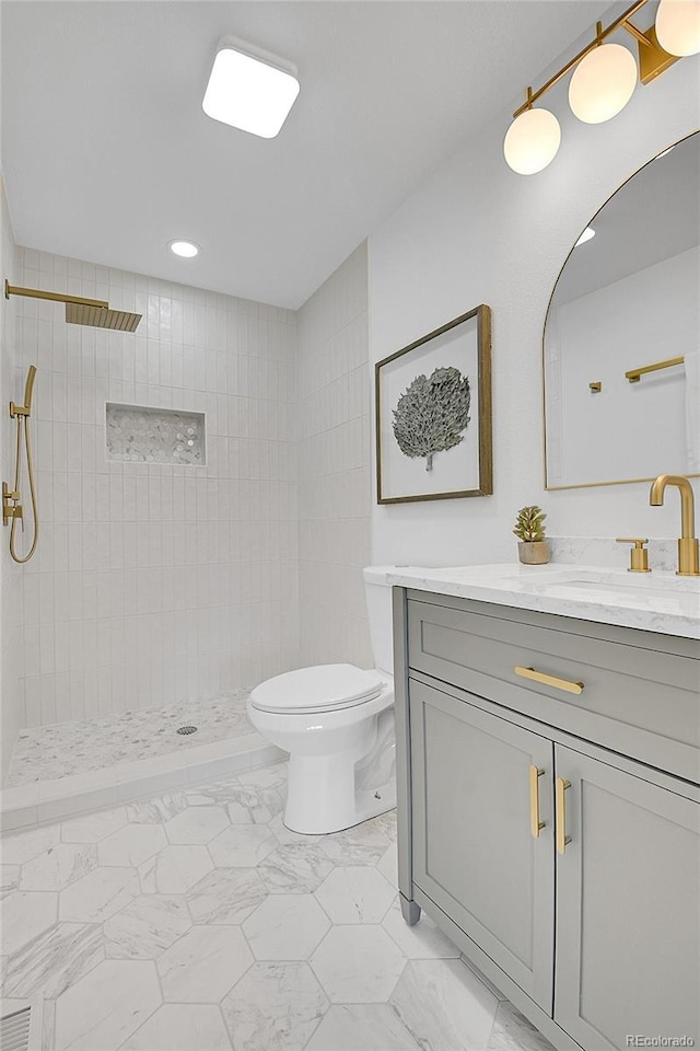 bathroom with toilet, marble finish floor, vanity, and a tile shower