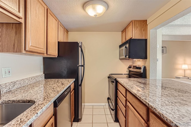 kitchen with light stone counters, light tile patterned flooring, appliances with stainless steel finishes, and a textured ceiling