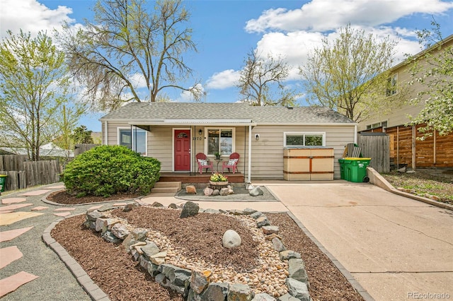 ranch-style home with concrete driveway, a shingled roof, a porch, and fence