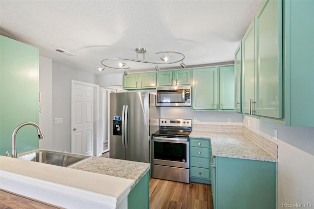 kitchen featuring green cabinets, visible vents, a sink, wood finished floors, and stainless steel appliances