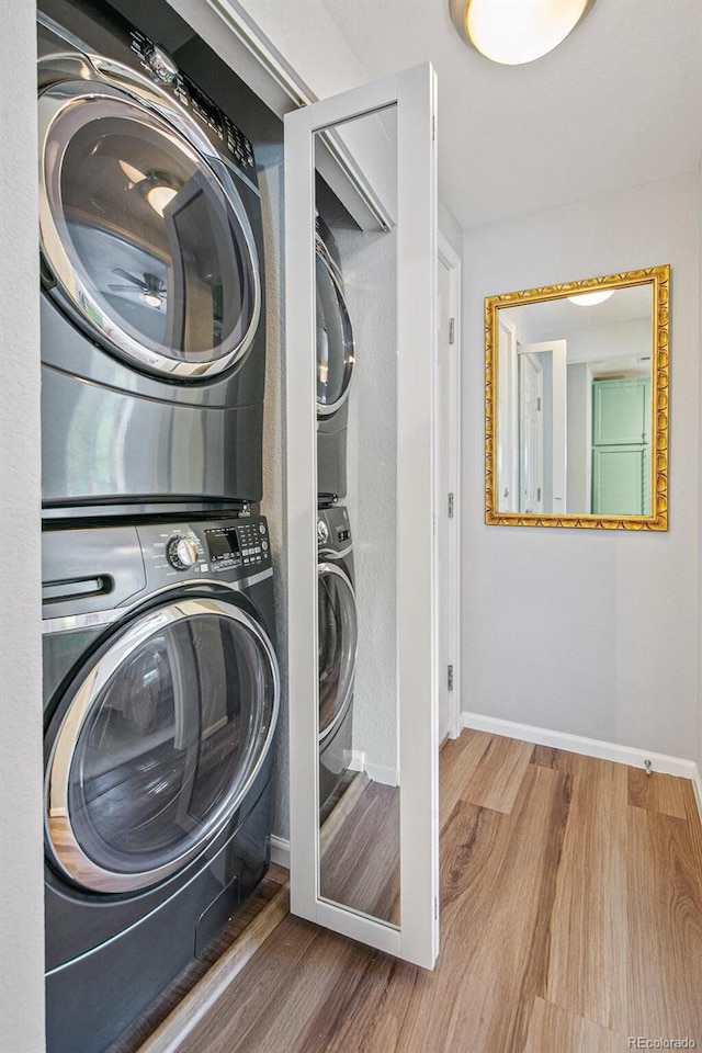 laundry area featuring laundry area, stacked washer / drying machine, baseboards, and wood finished floors