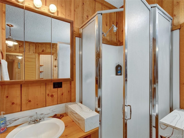 bathroom featuring a textured ceiling, a shower with door, sink, and wooden walls