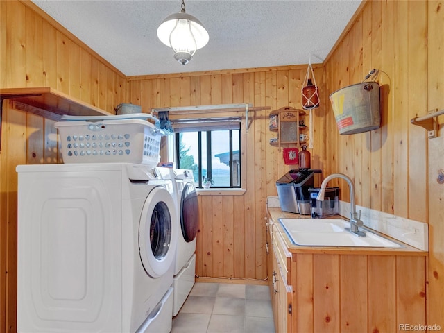 laundry room featuring wood walls, cabinets, sink, washer and dryer, and a textured ceiling