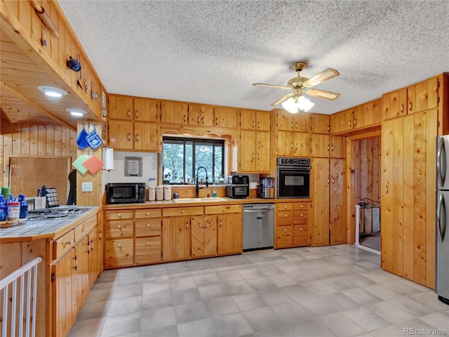 kitchen featuring tile countertops, wood walls, sink, and black appliances