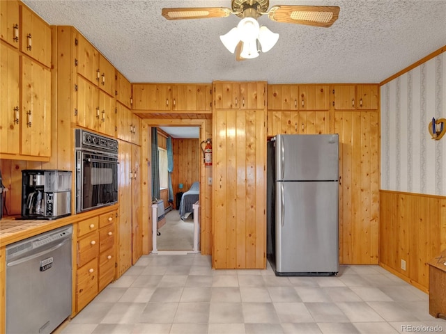 kitchen with a textured ceiling, stainless steel appliances, ceiling fan, and wooden walls