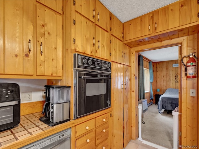 kitchen with a textured ceiling, wooden walls, tile countertops, dishwasher, and oven