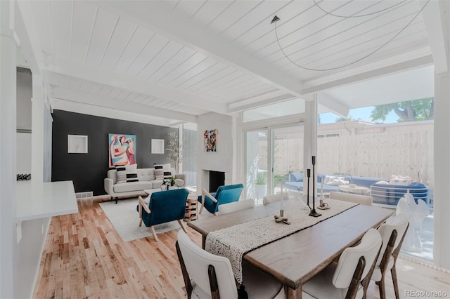 dining space featuring a fireplace, beamed ceiling, wood ceiling, and light hardwood / wood-style flooring