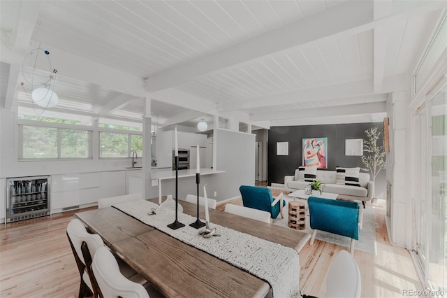 dining area with beamed ceiling, beverage cooler, sink, and light wood-type flooring