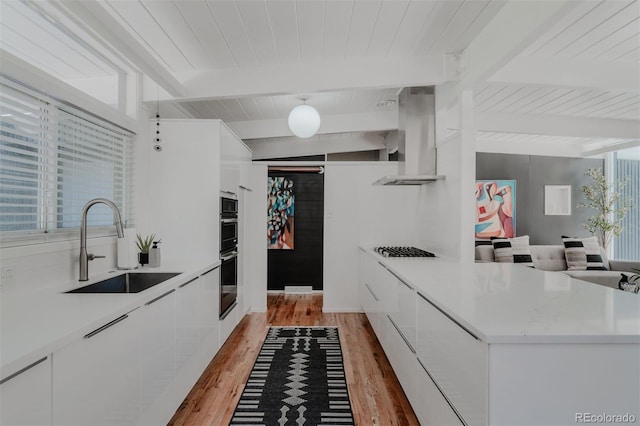 kitchen featuring beamed ceiling, sink, appliances with stainless steel finishes, white cabinets, and light wood-type flooring