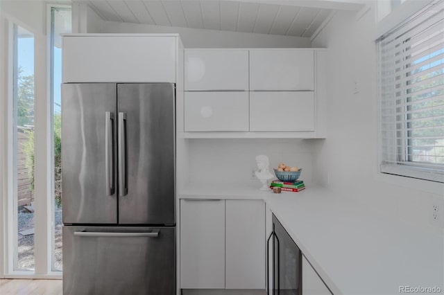 kitchen with white cabinetry, light wood-type flooring, stainless steel refrigerator, beverage cooler, and lofted ceiling