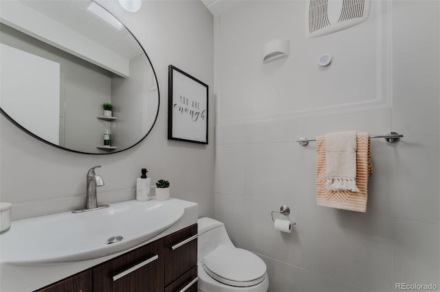 bathroom with toilet, vanity, and tile walls