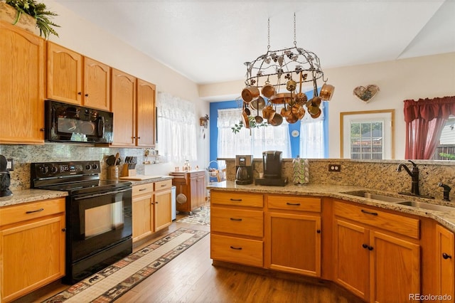 kitchen with light stone countertops, black appliances, hardwood / wood-style floors, and sink