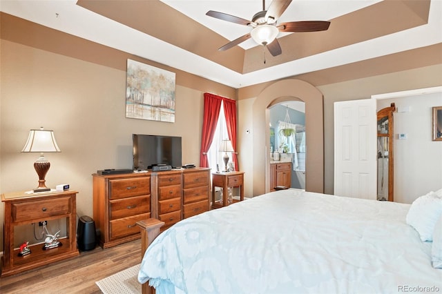 bedroom featuring light hardwood / wood-style flooring, connected bathroom, ceiling fan, and a raised ceiling