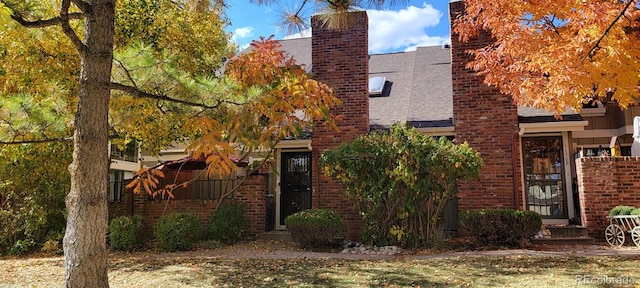 view of front facade with brick siding, roof with shingles, and a chimney