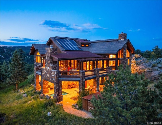 back house at dusk with a balcony, a patio, and solar panels