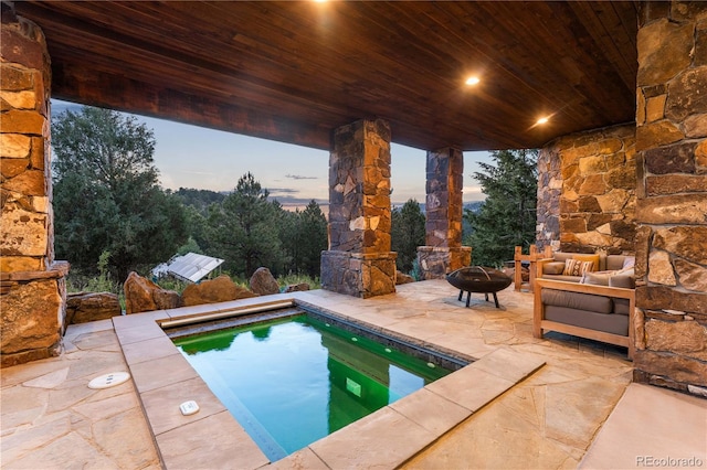 pool at dusk featuring an outdoor living space with a fire pit and a patio area