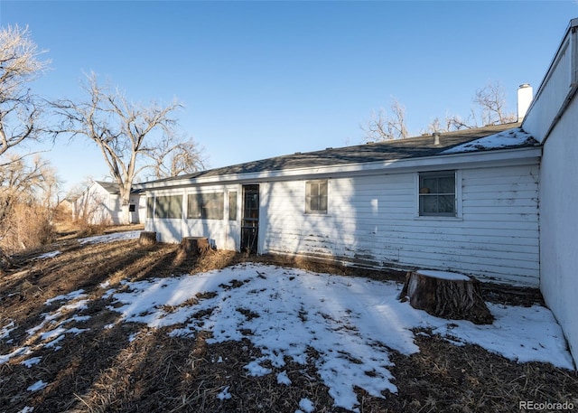 snow covered rear of property featuring a sunroom